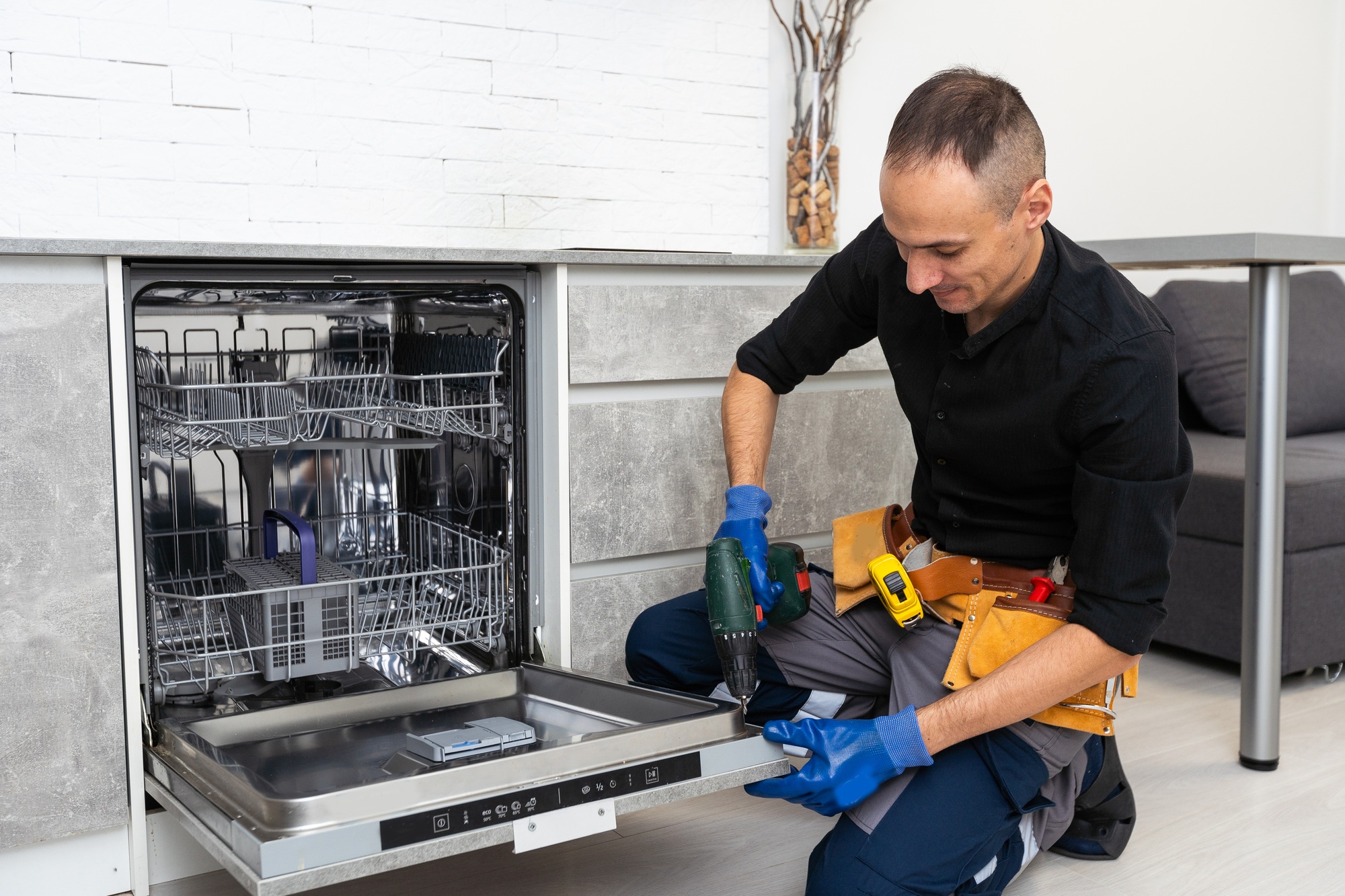 A plumber repairs a dishwasher in a kitchen room. Plumbing services.
